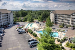 A hotel with a swimming pool, parking lot, and surrounding greenery.
