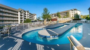 A swimming pool with a curved design, surrounded by a white fence and shaded by trees. - Whispering Pines 433 (Pigeon Forge)