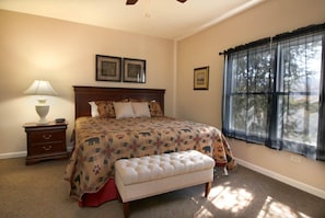 A bedroom with a bed, a nightstand, a lamp, a window with curtains, and a ceiling fan. - Whispering Pines 513 (Pigeon Forge)