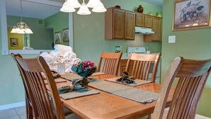 A dining room with a wooden table and chairs, a chandelier, and kitchen cabinets in the background. - Whispering Pines 521 (Pigeon Forge)