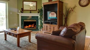 A living room with a fireplace, leather sofa, wooden cabinet, and a clock on the wall. - Whispering Pines 521 (Pigeon Forge)