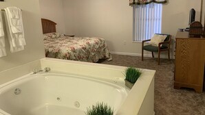 Ein Schlafzimmer mit einer großen Badewanne, einem Bett mit floralem Bettzeug, einem Sessel und einem Holzschrank.