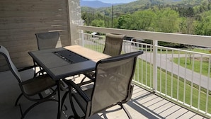 Ein Balkon mit Tisch und Stühlen, mit Blick auf eine grüne Landschaft und eine Straße.