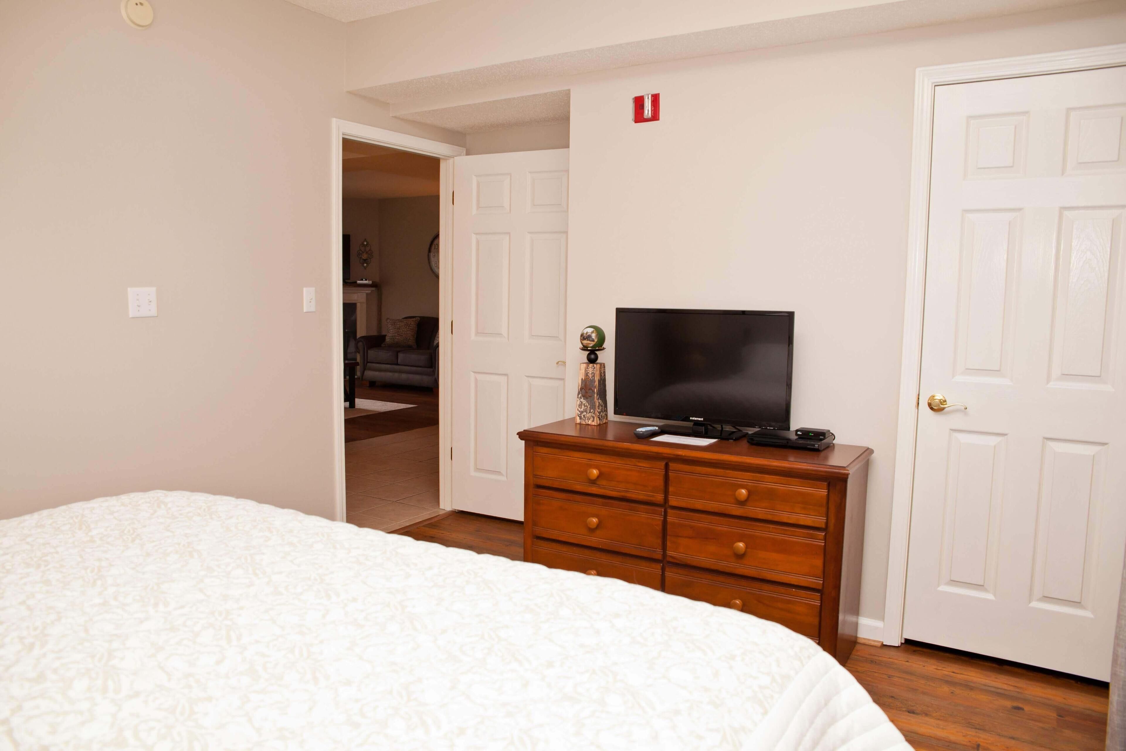 Een slaapkamer met een bed, een dressoir met televisie en een deur met rookmelder.