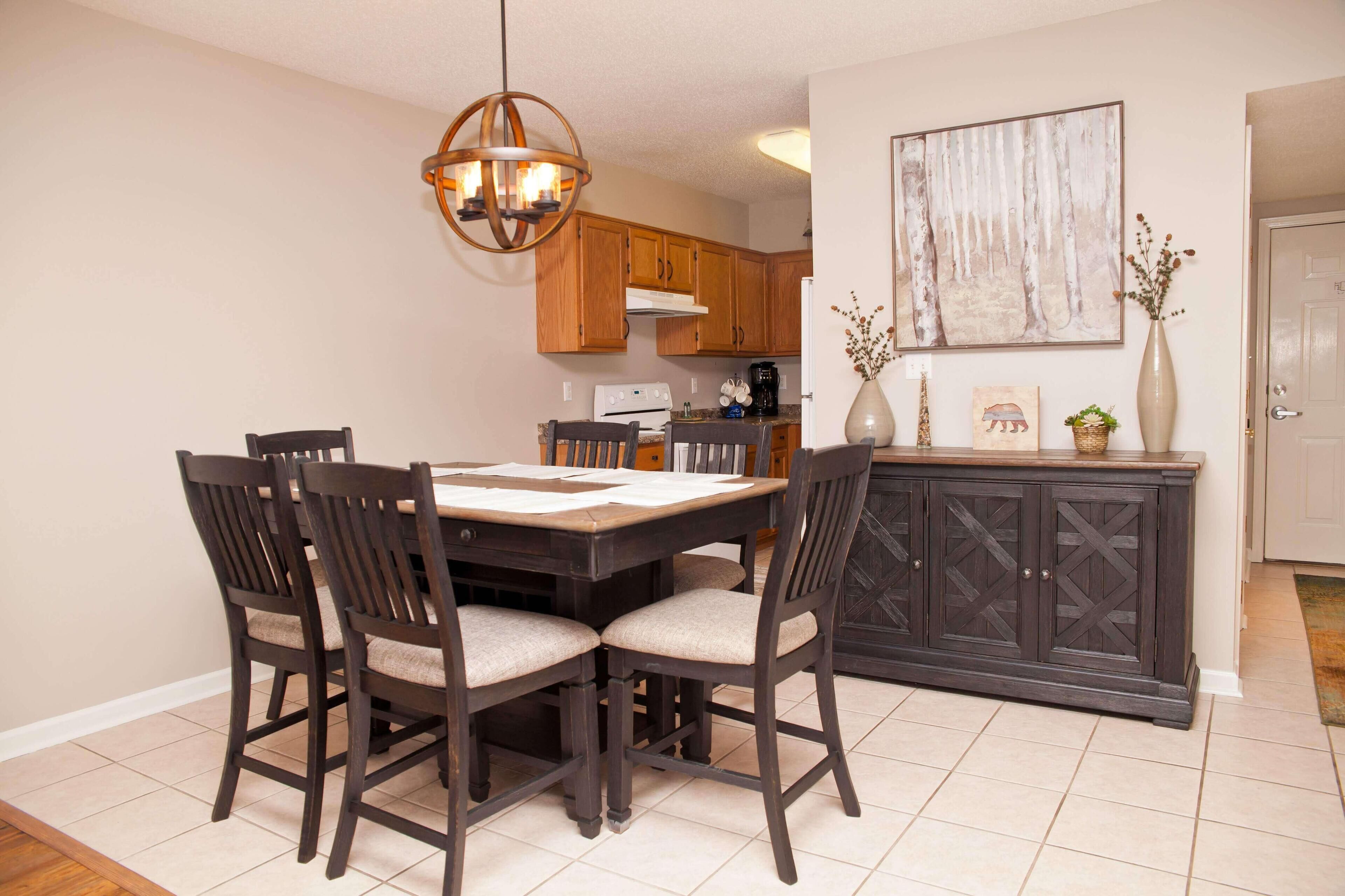 A dining area with a wooden table and chairs, a dark cabinet, and a hanging light fixture.