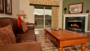 A living room with a leather sofa, a wooden coffee table, a fireplace, and a view through a large window with curtains.