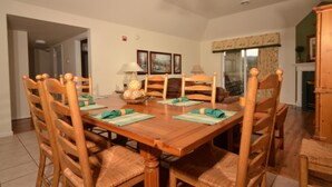 A dining room with a wooden table and chairs, a chandelier, and framed artwork on the wall.