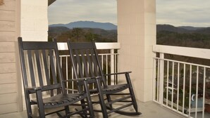 A balcony with two black rocking chairs, white railings, and a view of distant mountains.
