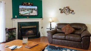 Ein Wohnzimmer mit Kamin, einer Ledersofa, einem Couchtisch und einem an einer grünen Wand befestigten Fernseher.