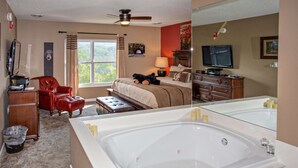 Camera d'albergo con una grande vasca da bagno bianca, un letto con un orsetto di peluche, una poltrona in pelle rossa, una scrivania con un computer e una televisione.