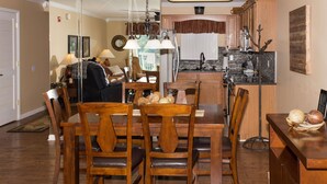 Zona pranzo con arredi in legno, un lampadario e una cucina sullo sfondo.