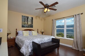 A bedroom with a large bed, a ceiling fan, a window with a view, and a nightstand with a lamp. - Whispering Pines 454 (Pigeon Forge)