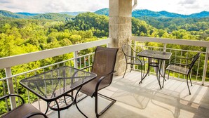 A balcony with outdoor furniture, a stone pillar, and a view of a forested mountain range. - Whispering Pines 451 (Pigeon Forge)