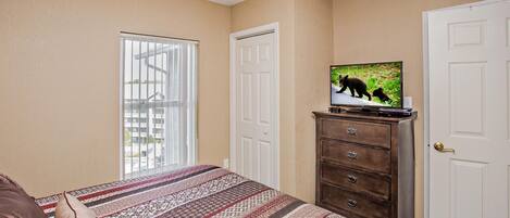 A bedroom with a bed, a dresser, a television, and a window with blinds.