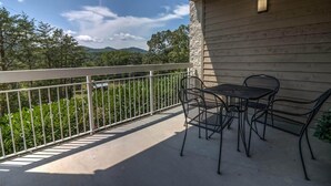A balcony with a table and chairs, a stone wall, and a view of greenery and hills. - Whispering Pines 612 (Pigeon Forge)
