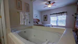 A bathroom with a large bathtub, a ceiling fan, and a window with curtains. - Whispering Pines 612 (Pigeon Forge)