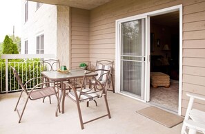 A patio with a table and chairs, a sliding glass door, and a small step leading to a covered area.