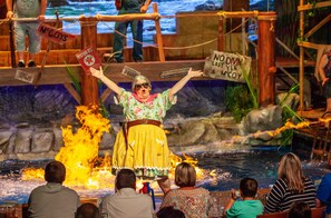 A stage performance with a performer in a floral dress and a fire effect in the background.