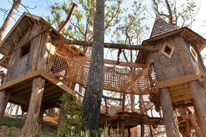 Una construcció de casa d'arbos amb pont de corda, envoltada d'arbres.