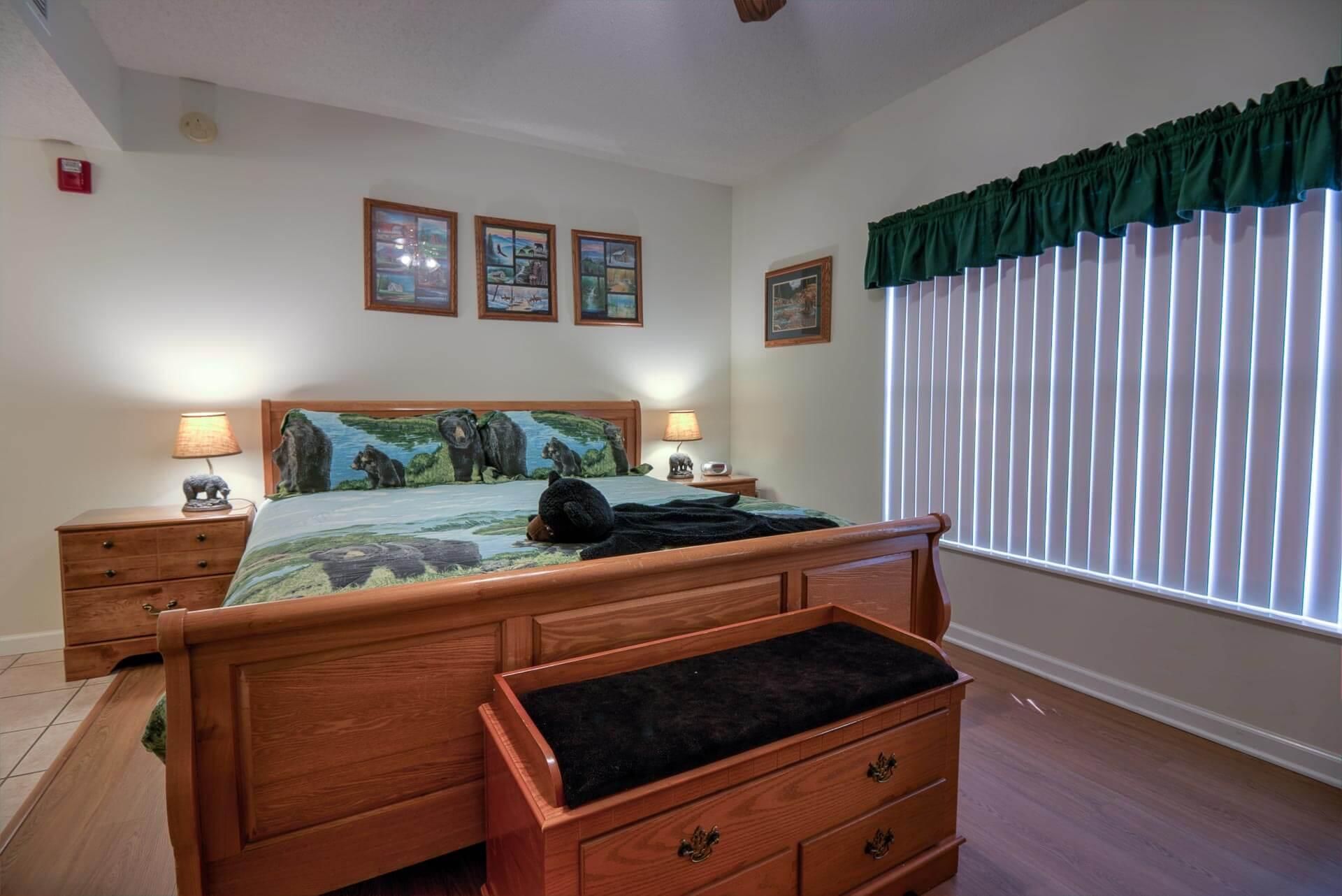 A bedroom with a wooden bed, two bedside tables, a nightstand, a green curtain, and three framed pictures on the wall.