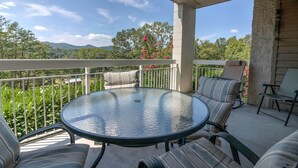 Une terrasse extérieure couverte, dotée d’une table ronde en verre et de chaises à coussins rayés.