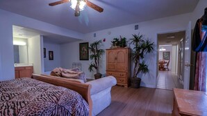 Une chambre à coucher avec un lit, une armoire et un ventilateur de plafond. On aperçoit, à l’arrière-plan, des plantes en pot et un coin repas.