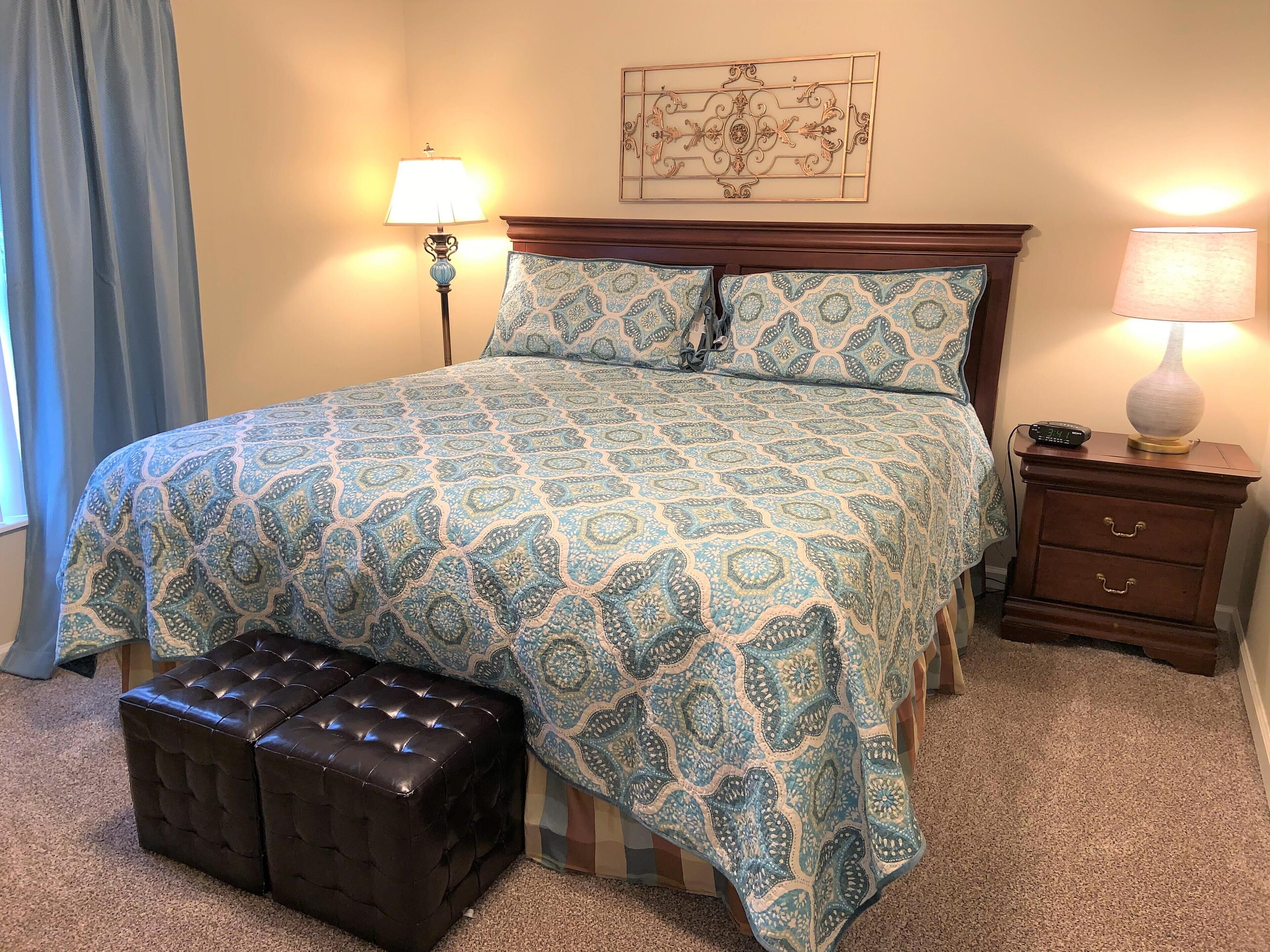 A neatly made bed with patterned bedding, a bedside table with a lamp, and a decorative wall piece.