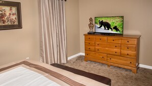 Une chambre à coucher avec un lit, une commode en bois, un téléviseur qui diffuse une image d’un ours et un rideau.