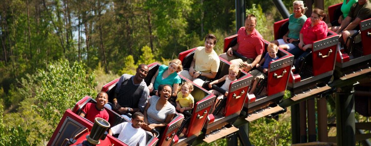 A group of people on a wooden roller coaster with red cars.