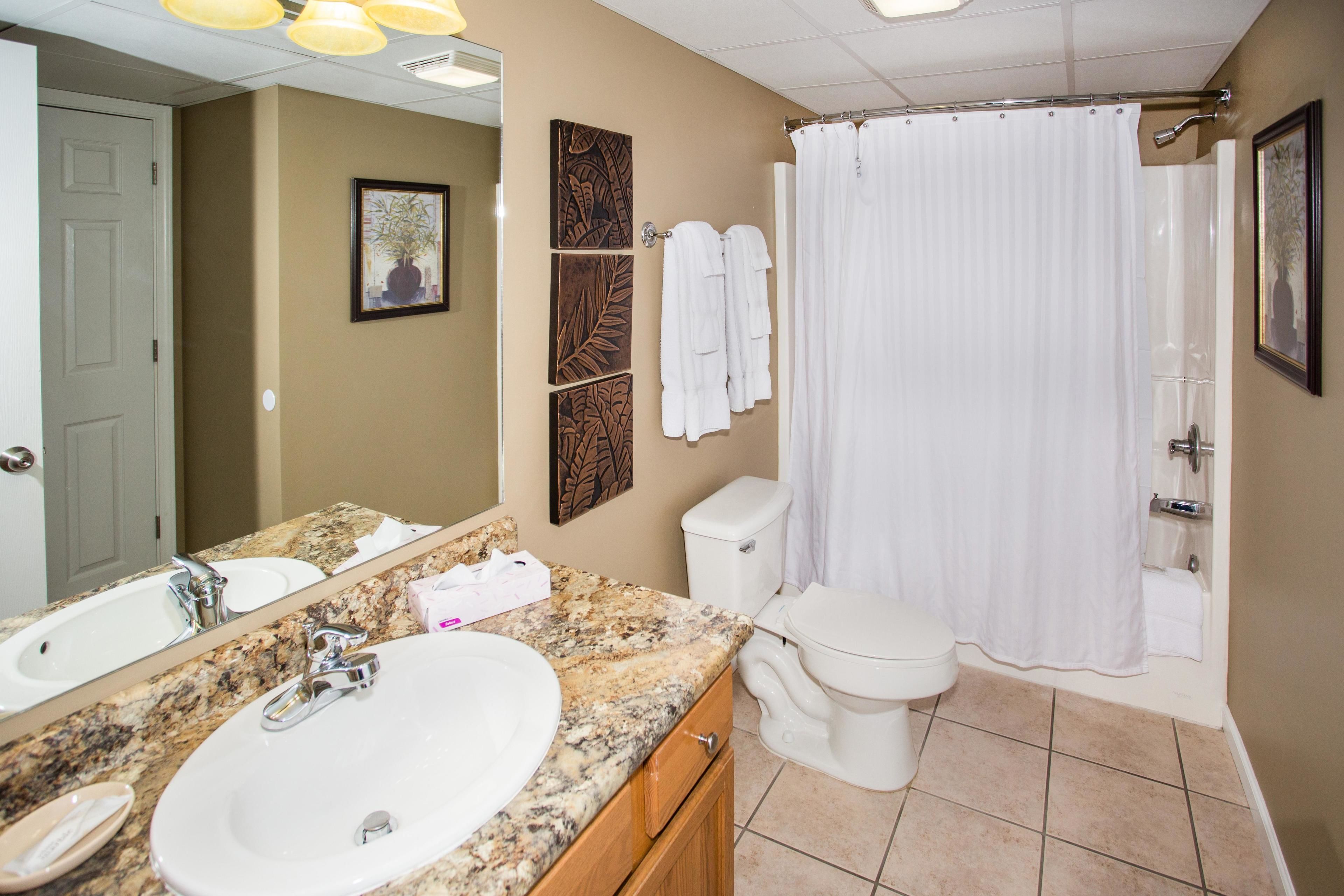 A bathroom with a granite countertop sink, a toilet, a shower curtain, and a mirror.