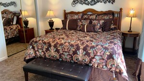 Een slaapkamer met een groot bed, twee nachtkastjes met lampen, een bankje en een decoratief wandobject.