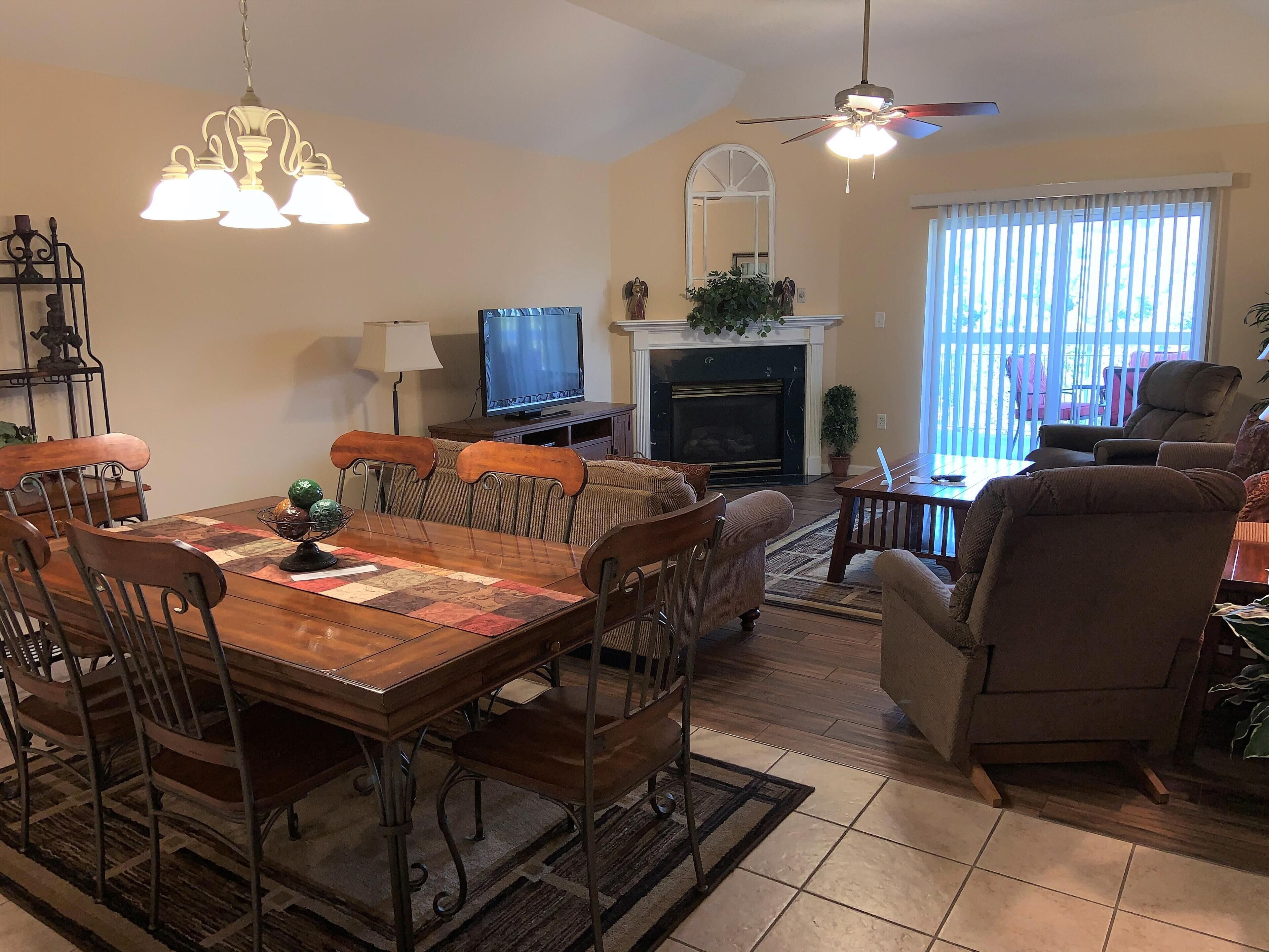 A living room with a wooden dining table, chairs, a fireplace, a television, and a ceiling fan.