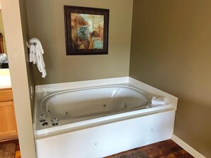 Un baño con una bañera blanca, una obra de arte enmarcada encima y un perchero con toallas.