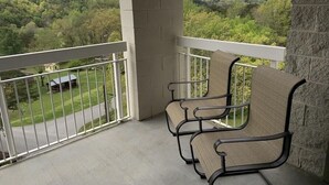 Un balcón con dos sillas, vista a un paisaje verde y una montaña al fondo.