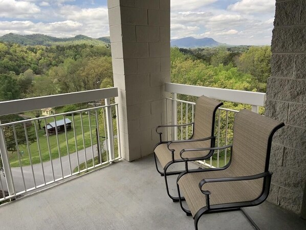 Un balcón con dos sillas, vista a un paisaje verde y una montaña al fondo.