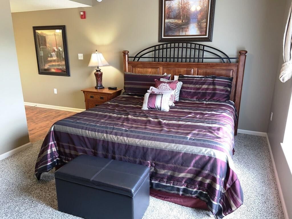 A bedroom with a bed, a nightstand, a lamp, and a framed picture on the wall.