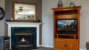 A living room with a fireplace, a television on a wooden stand, and a mirror above the fireplace. - Whispering Pines 634 (Pigeon Forge)