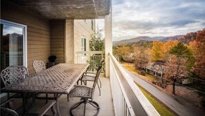 A balcony with a table and chairs, overlooking a scenic view of autumn foliage and distant hills. - Whispering Pines 634 (Pigeon Forge)