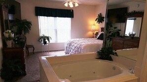 A bedroom with a large bathtub, a bed, a dresser, a mirror, and a window with curtains. - Whispering Pines 643 (Pigeon Forge)