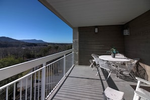 A balcony with a table and chairs, overlooking a scenic landscape with mountains and trees. - Whispering Pines 654 (Pigeon Forge)