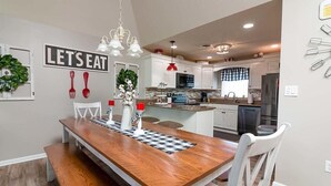 Een moderne keuken met witte kasten, een houten eettafel en een bord waarop staat 'LET'S EAT'.