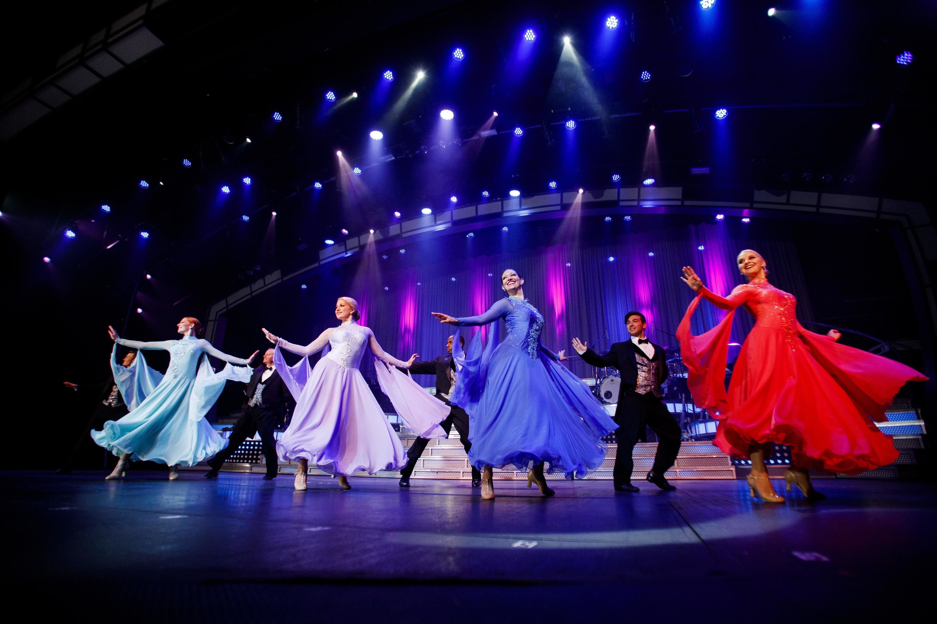 Een podium waarop dansers in verschillende gekleurde jurken optreden.