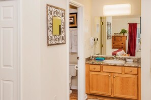 Une salle de bain avec un meuble-lavabo en bois, un évier et un miroir. On y trouve également un porte-serviettes et une plante en pot sur le meuble-lavabo.