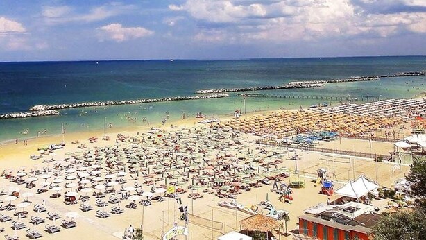 A beach with numerous umbrellas and sun loungers, a clear sky, and a calm sea. - Hotel Villa Iris (Rimini)