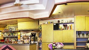 A bar area with shelves of bottles, a counter with a vase of flowers, and a ceiling fan. - Hotel Villa Iris (Rimini)