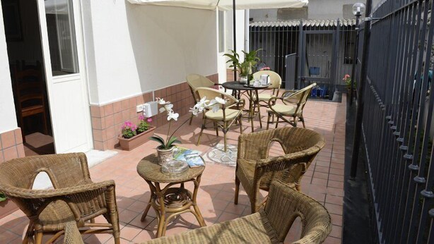 Un patio al aire libre con mobiliario de mimbre, una sombrilla blanca y plantas en macetas.
