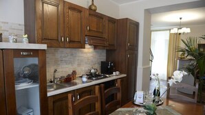 Una cocina con armarios de madera, un salpicadero de azulejos, una estufa y un comedor con una mesa para dos.