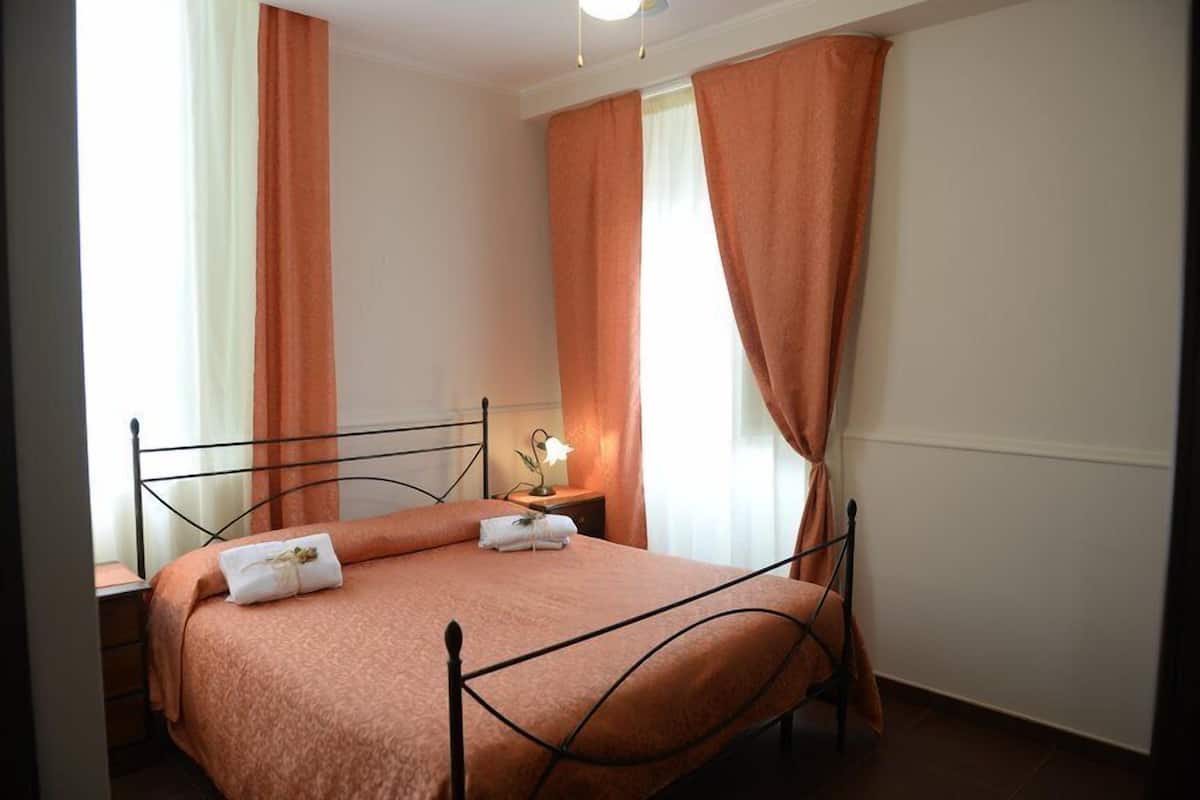 A single bed with a metal frame, a bedside table with a lamp, and curtains.