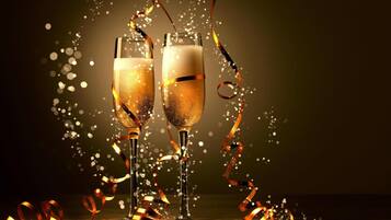 Zwei Sektgläser mit goldener Flüssigkeit, umgeben von goldenen Girlanden und Bläschen, was eine festliche Stimmung vermittelt.