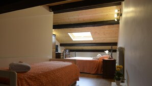 Un dormitorio con dos camas, un tragaluz, un radiador y una pequeña mesa con flores.